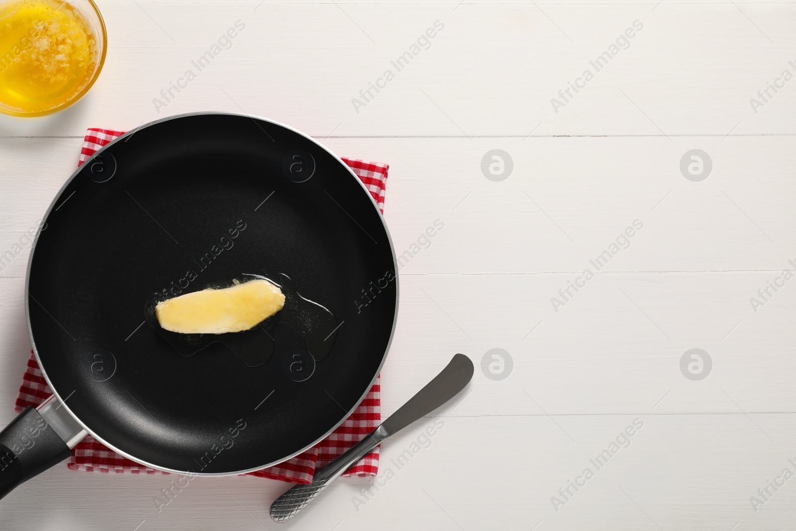 Photo of Melting butter in frying pan and knife on white wooden table, top view. Space for text