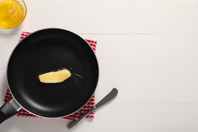 Photo of Melting butter in frying pan and knife on white wooden table, top view. Space for text