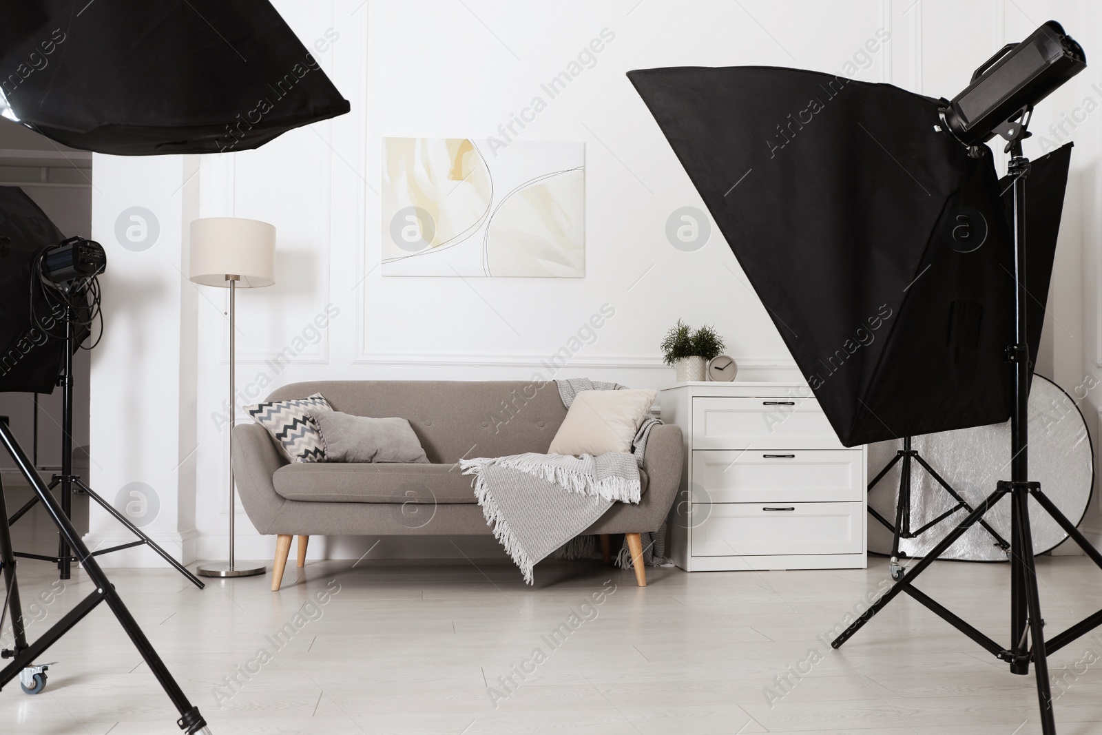 Photo of Set of stylish furniture surrounded by professional lighting equipment in photo studio. Cozy living room interior imitation
