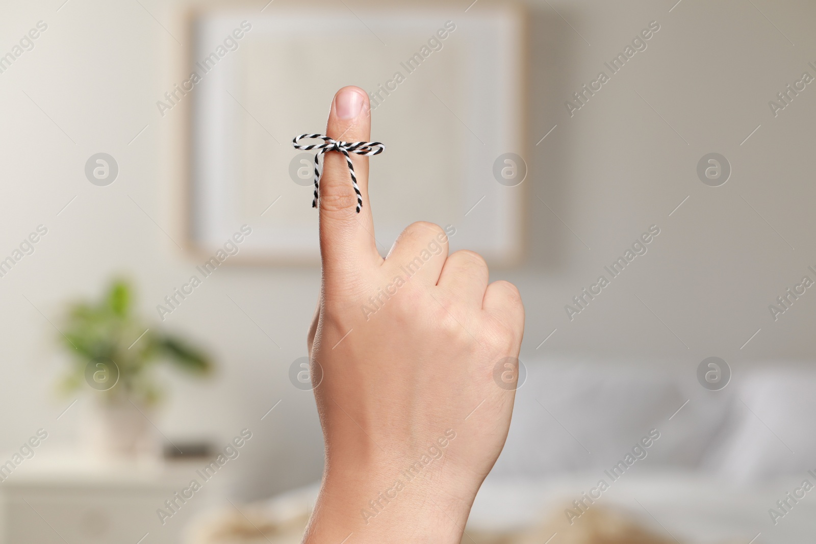 Photo of Man showing index finger with tied bow as reminder indoors, closeup