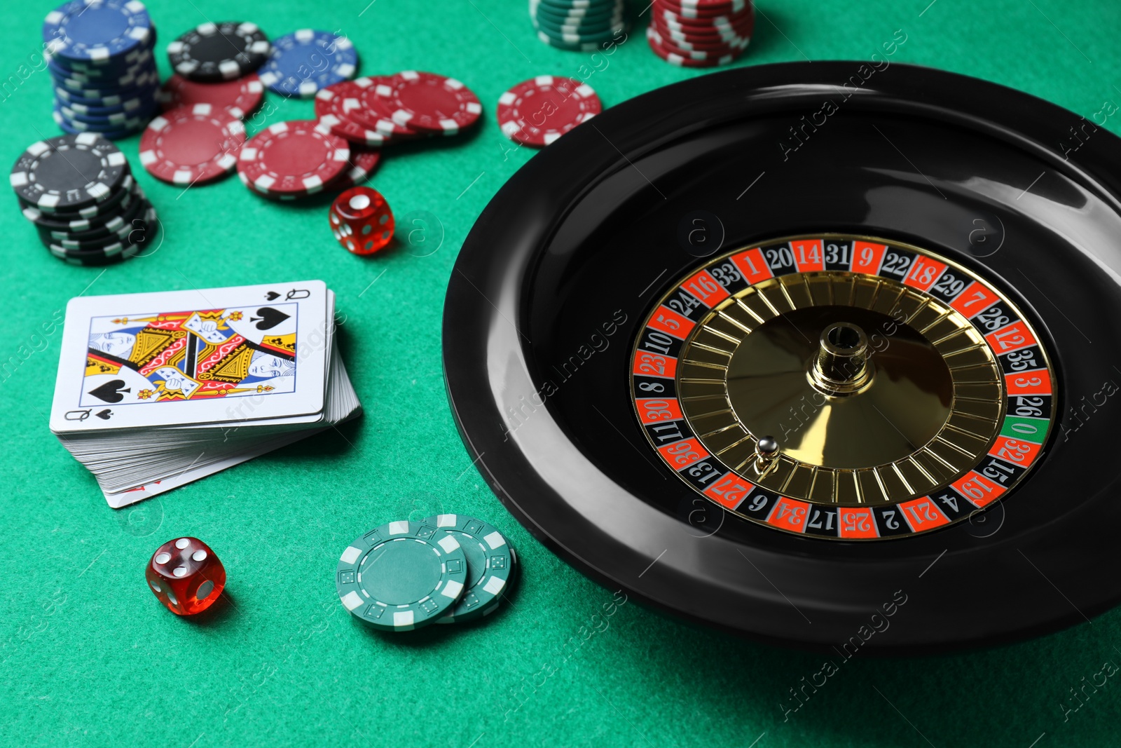 Photo of Roulette wheel, playing cards, chips and dice on green table, closeup. Casino game