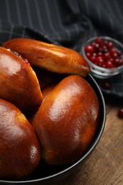 Photo of Delicious baked cranberry pirozhki in bowl on wooden table