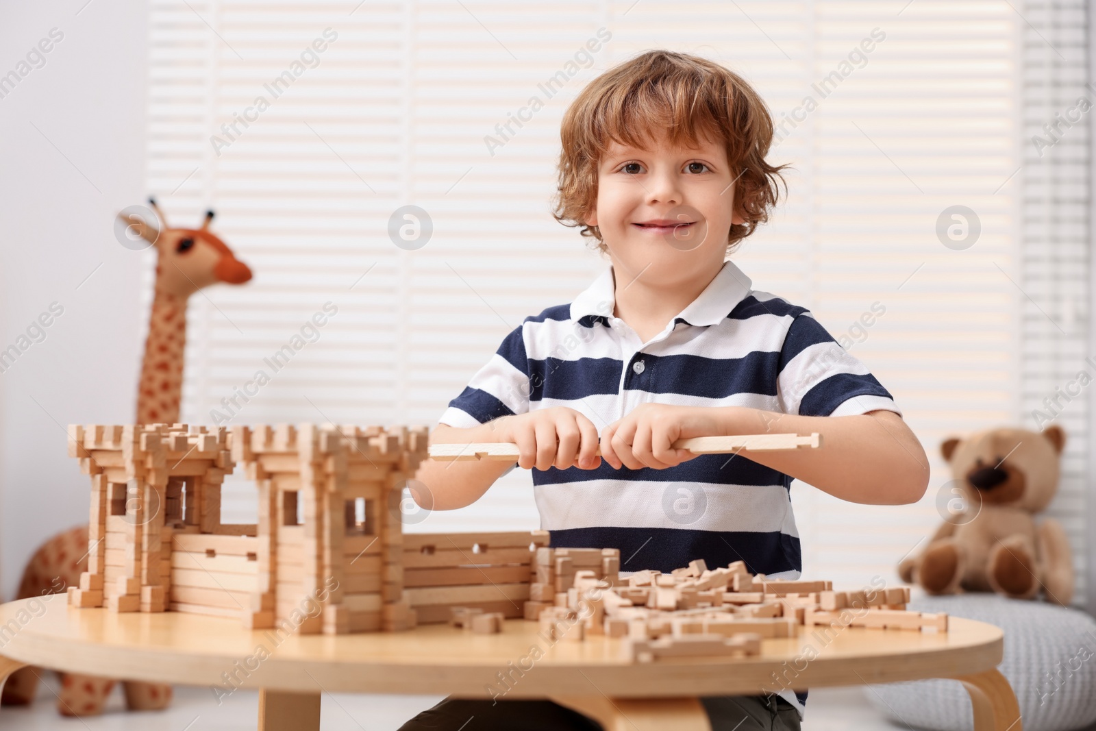 Photo of Cute little boy playing with wooden construction set at table in room. Child's toy