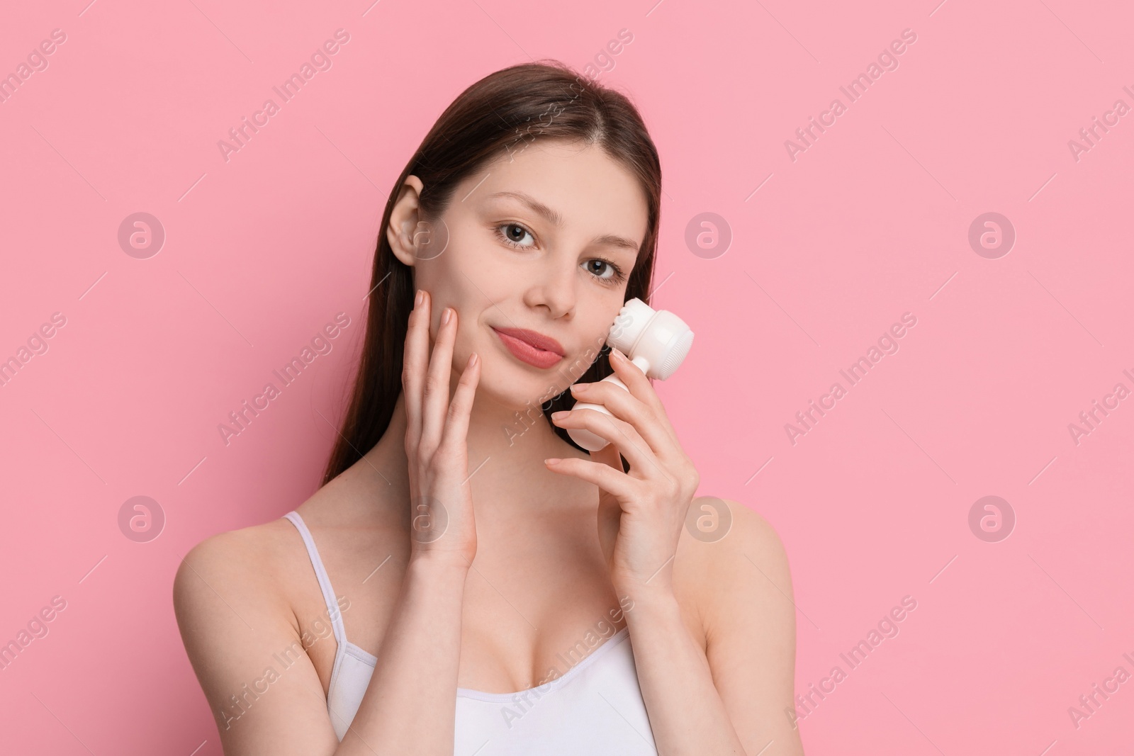 Photo of Washing face. Young woman with cleansing brush on pink background