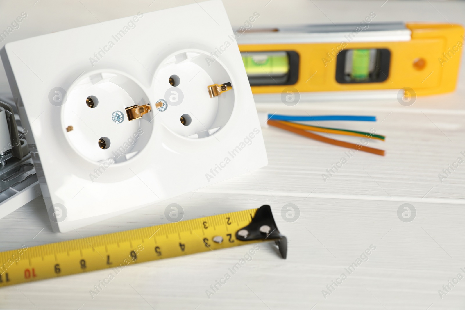 Photo of Power socket and set of electrician's tools on white wooden table, closeup