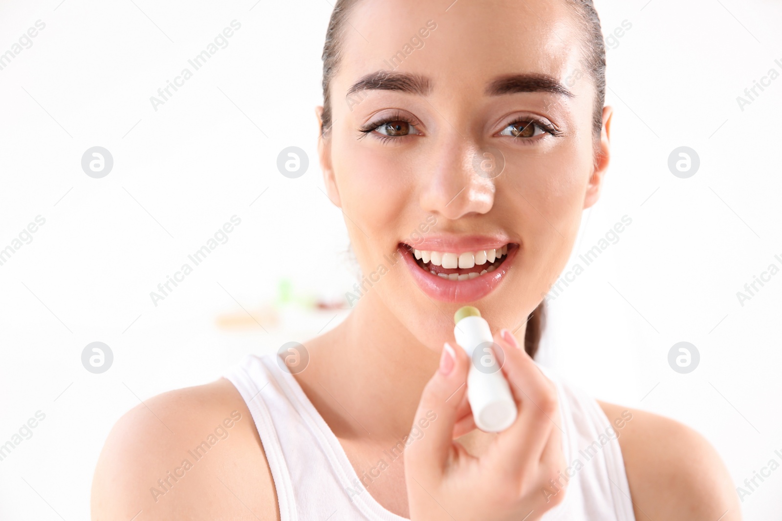 Photo of Young woman applying balm on her lips against light background