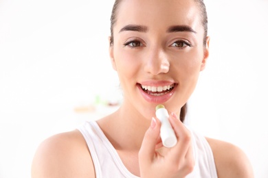 Photo of Young woman applying balm on her lips against light background