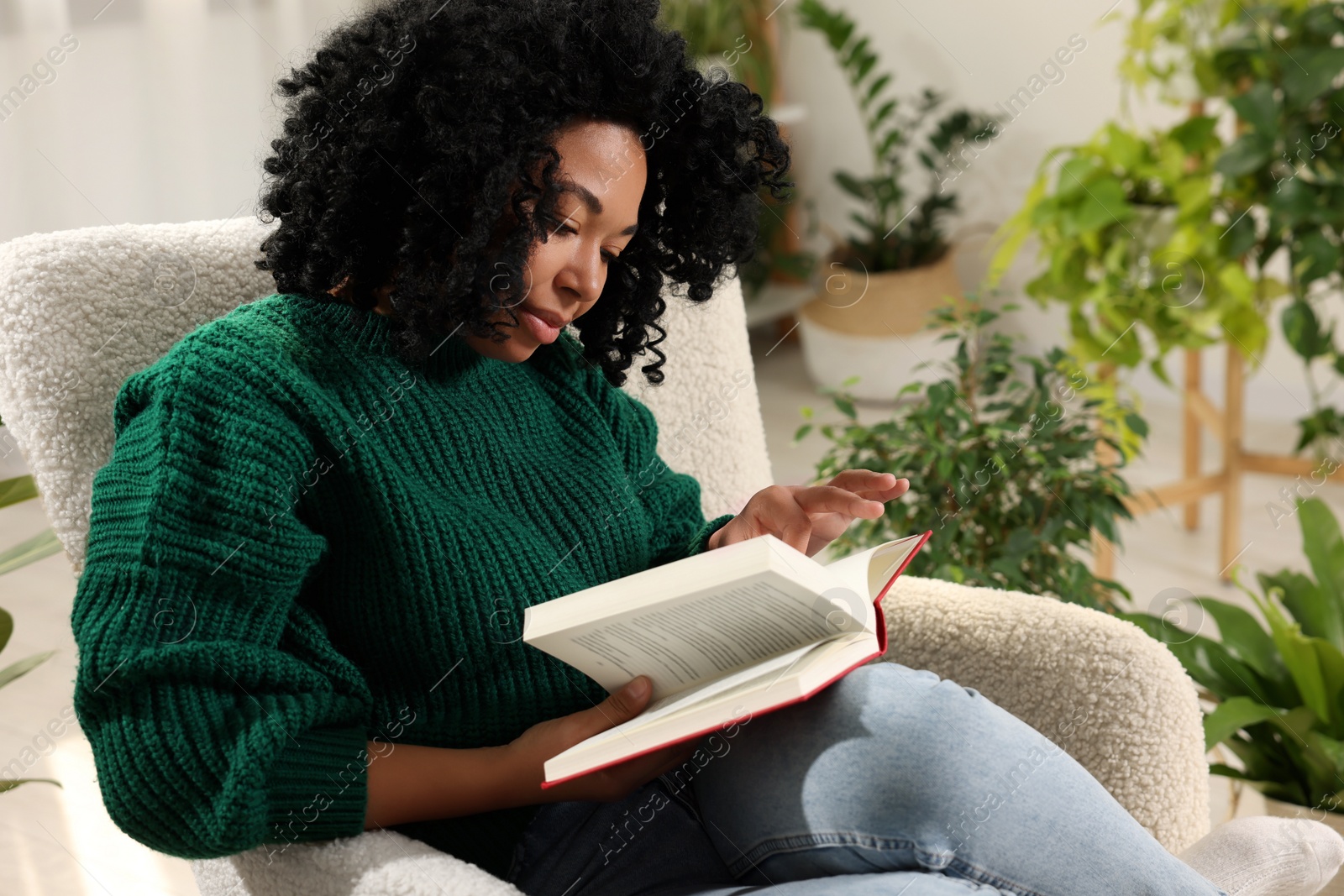 Photo of Relaxing atmosphere. Woman reading book in armchair in room with beautiful houseplants