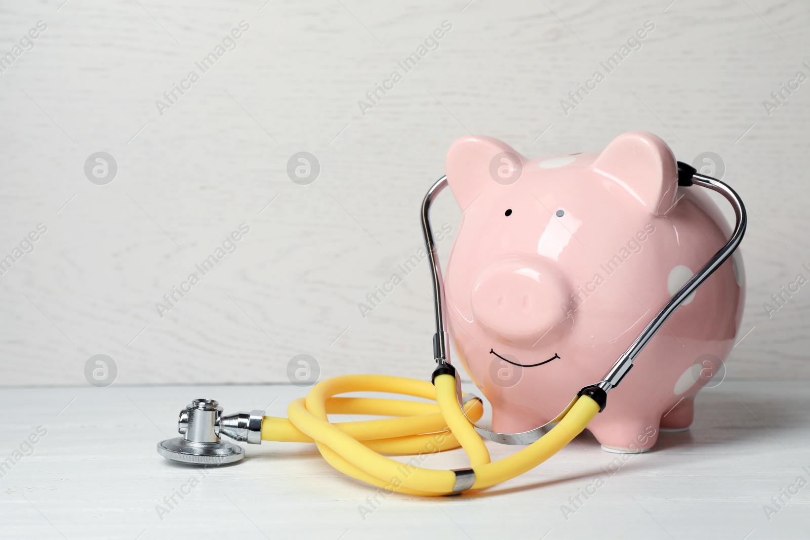 Photo of Piggy bank with stethoscope on light table. Space for text