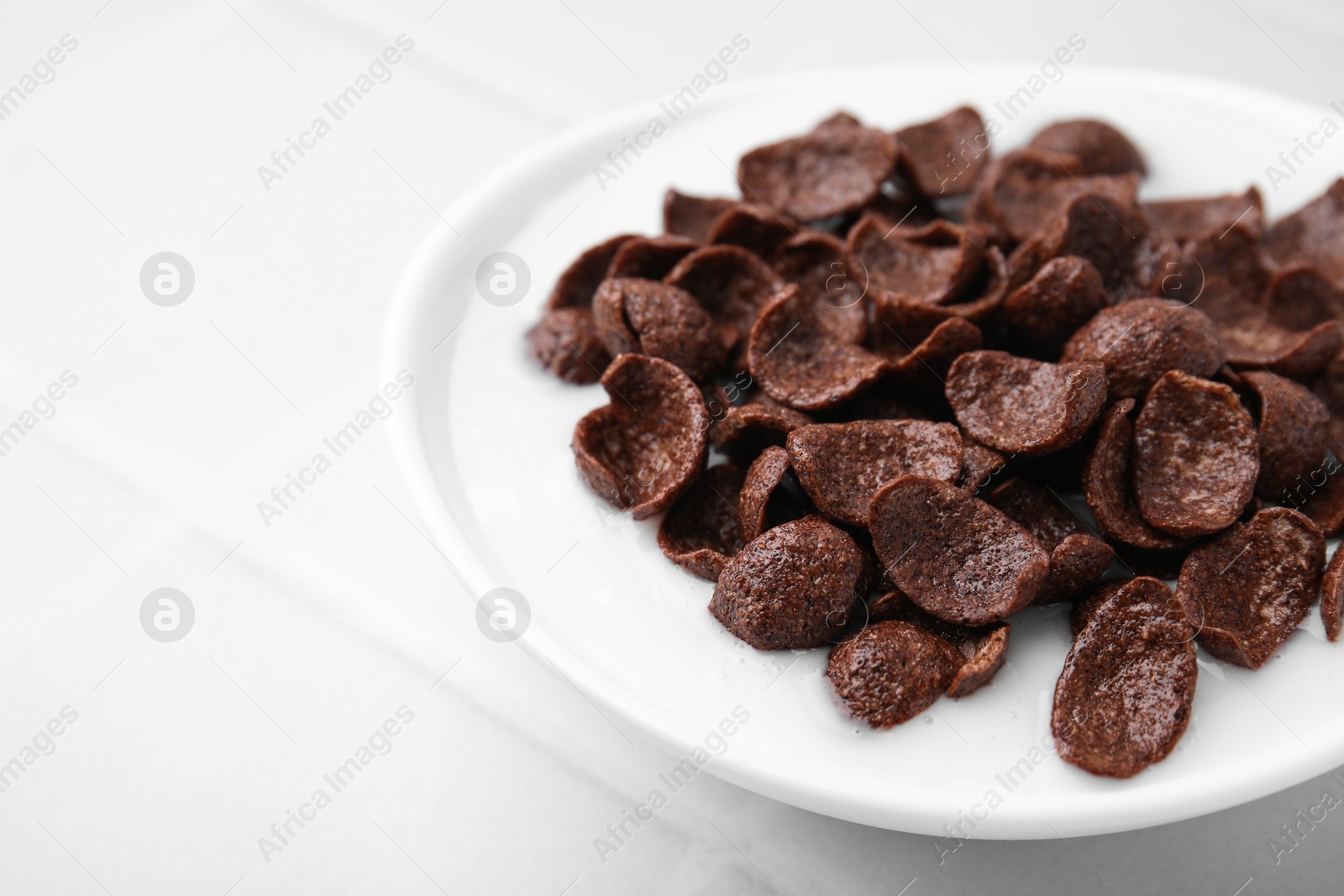 Photo of Breakfast cereal. Chocolate corn flakes and milk in bowl on white tiled table, closeup. Space for text