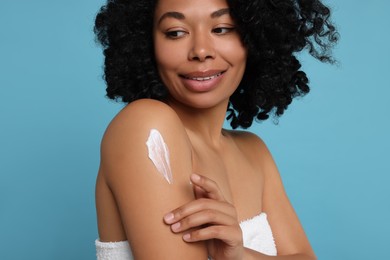 Photo of Young woman applying body cream onto shoulder on light blue background