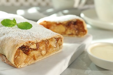 Photo of Delicious strudel with apples, nuts and powdered sugar on table, closeup. Space for text
