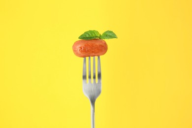 Fork with tasty fried sausage and basil leaves on yellow background