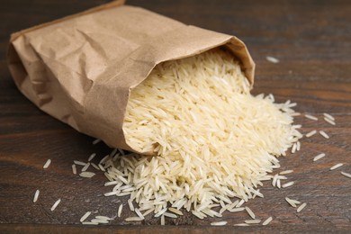 Photo of Overturned paper bag with raw rice on wooden table, closeup