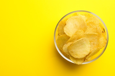 Delicious crispy potato chips in bowl on color background, top view with space for text