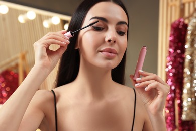 Photo of Beautiful young woman applying mascara in dressing room, closeup