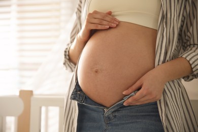 Photo of Pregnant woman touching her belly indoors, closeup