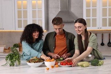 Photo of Friends cooking healthy vegetarian meal at white marble table in kitchen