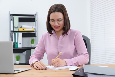 Happy young intern working at table in modern office