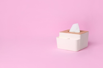 Photo of Holder with paper tissues on pink background. Space for text