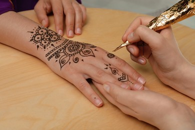 Photo of Master making henna tattoo on hand at wooden table, closeup. Traditional mehndi
