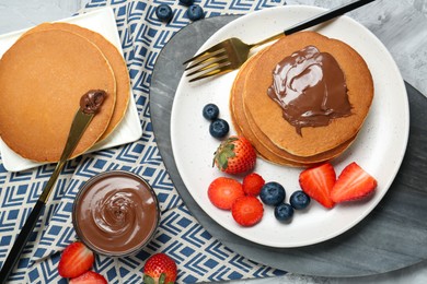 Photo of Tasty pancakes with chocolate paste and berries served on grey table, flat lay