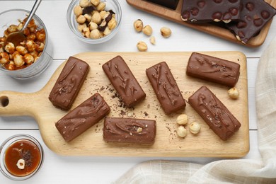 Photo of Delicious chocolate candy bars, caramel and nuts on white wooden table, flat lay