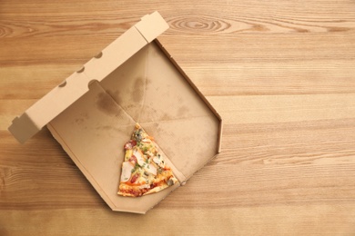 Cardboard box with pizza piece on wooden background, top view with space for text