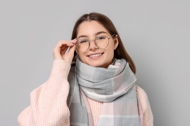 Beautiful woman in warm scarf and glasses on gray background