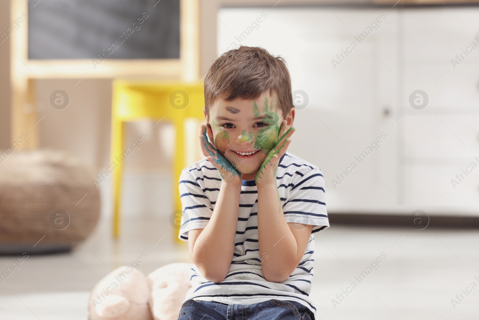 Photo of Happy little child with paint on face in room