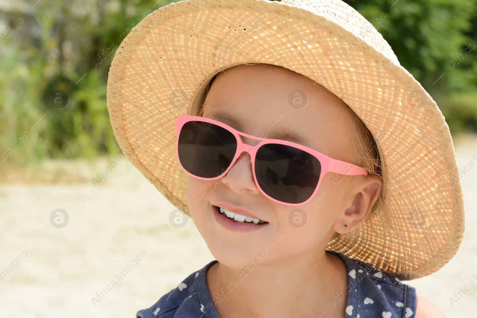 Photo of Little girl wearing sunglasses and hat at beach on sunny day