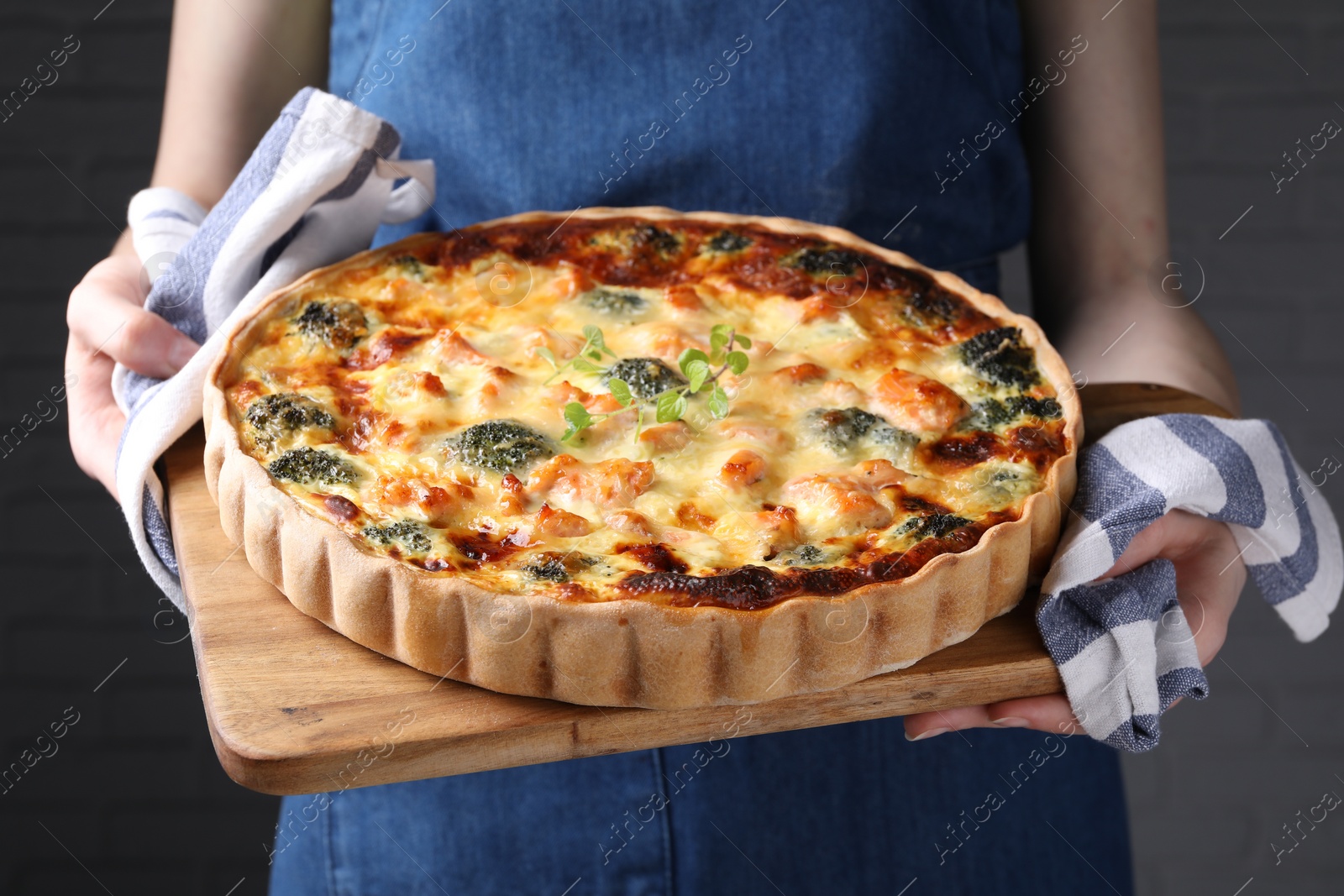 Photo of Woman holding wooden board with delicious homemade salmon quiche on gray background, closeup