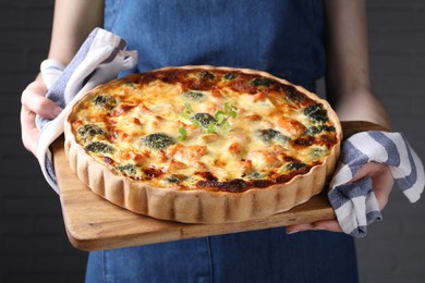 Photo of Woman holding wooden board with delicious homemade salmon quiche on gray background, closeup