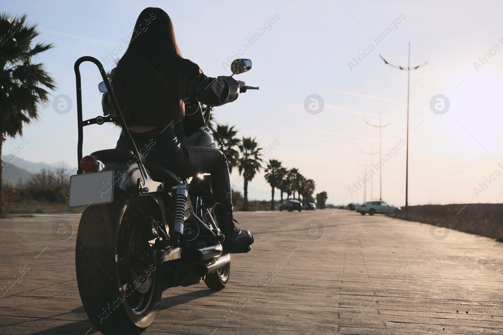 Photo of Woman riding motorcycle at sunset, back view. Space for text