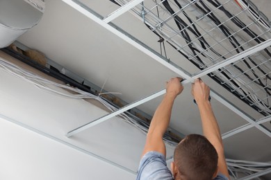 Photo of Worker installing metal frame indoors, closeup. Suspended ceiling