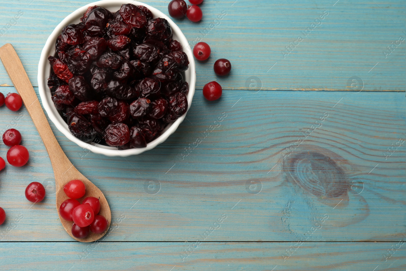 Photo of Tasty dried cranberries in bowl and fresh ones on light blue wooden table, top view. Space for text