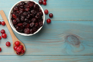 Tasty dried cranberries in bowl and fresh ones on light blue wooden table, top view. Space for text