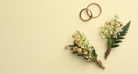 Small stylish boutonnieres and rings on beige background, flat lay. Space for text
