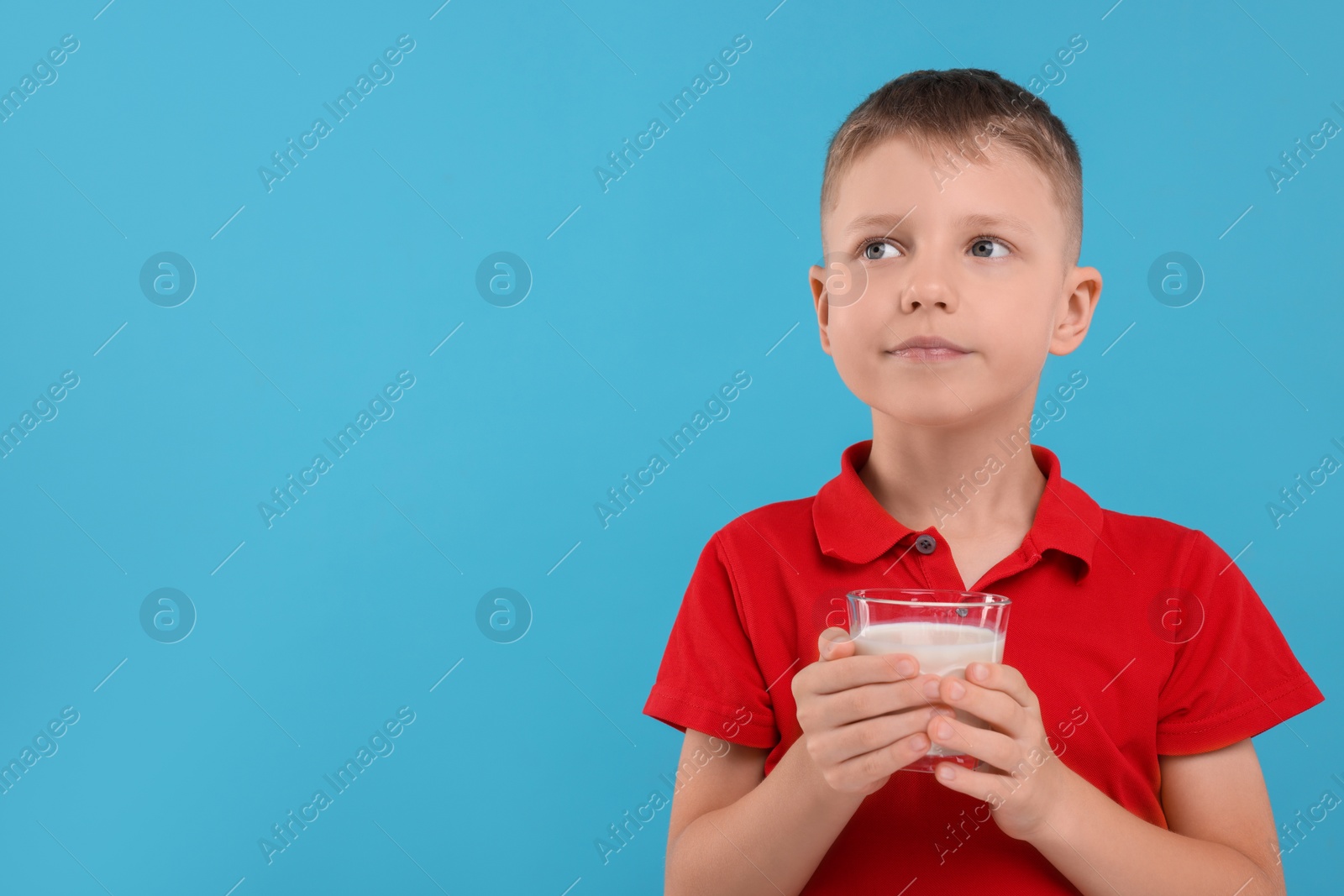 Photo of Cute boy with glass of fresh milk on light blue background, space for text