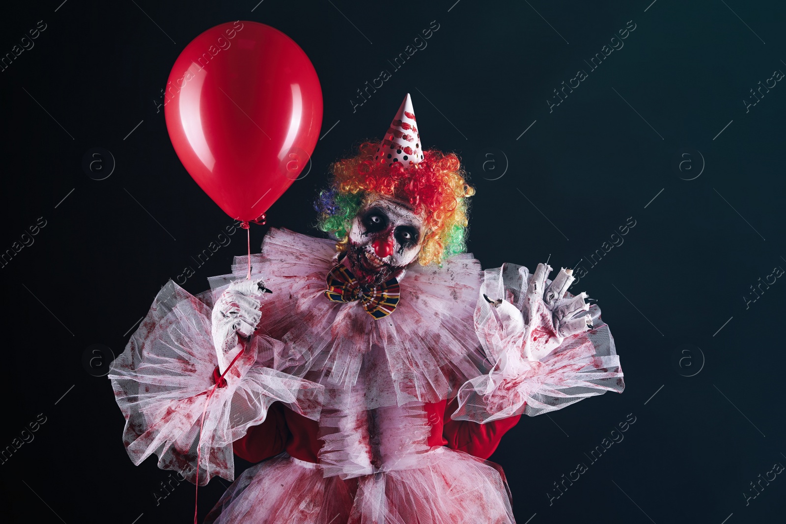 Photo of Terrifying clown with red air balloon on black background. Halloween party costume