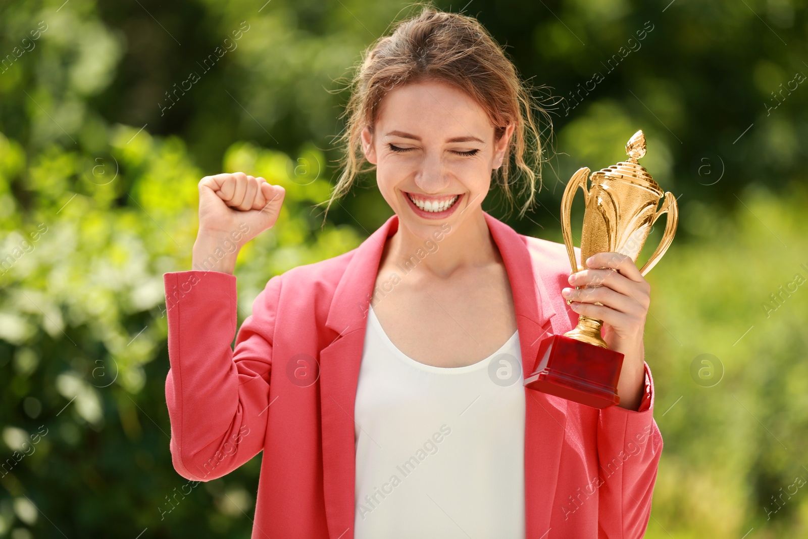 Photo of Portrait of happy young businesswoman with gold trophy cup in green park