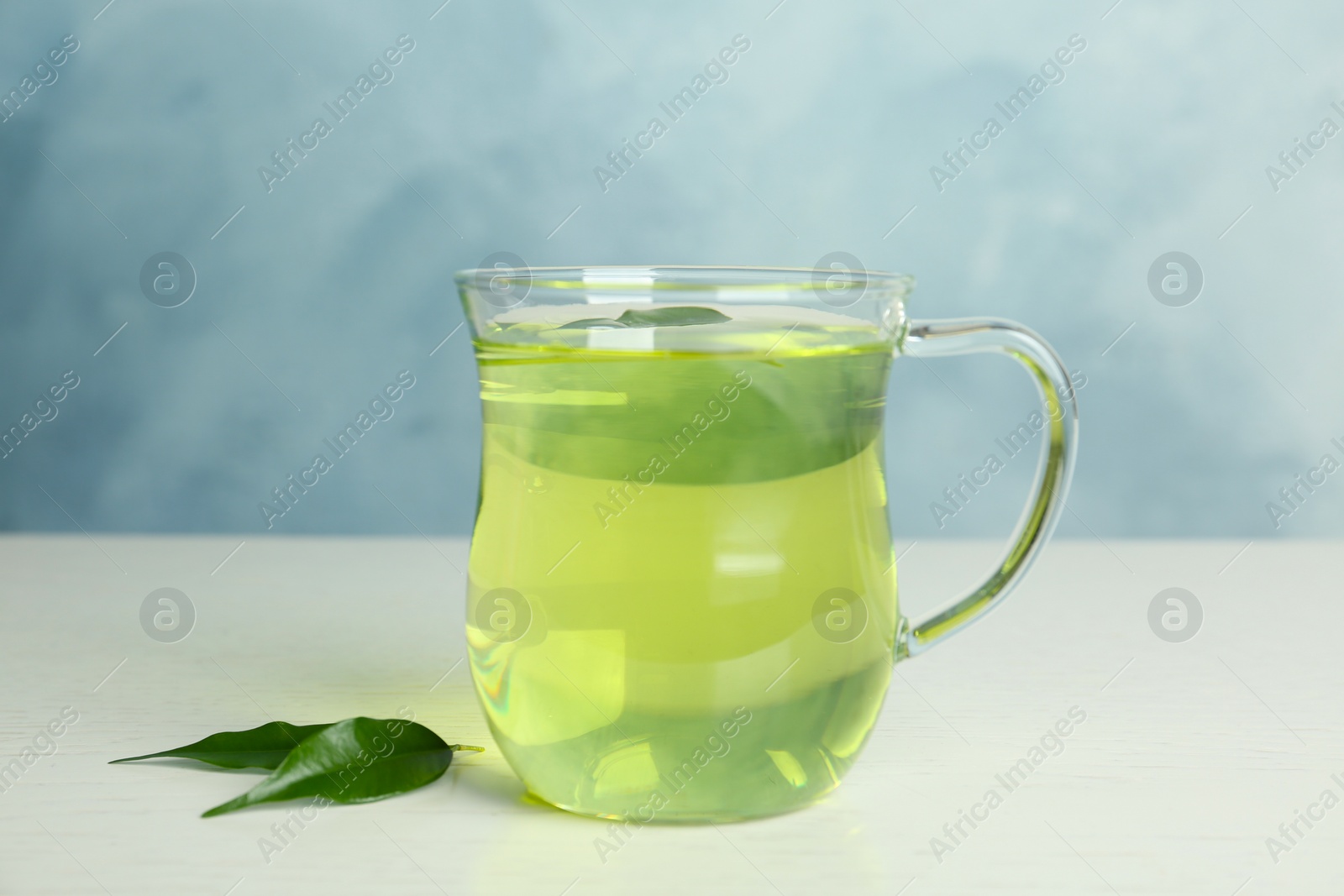 Photo of Cup of aromatic green tea and leaves on light wooden table