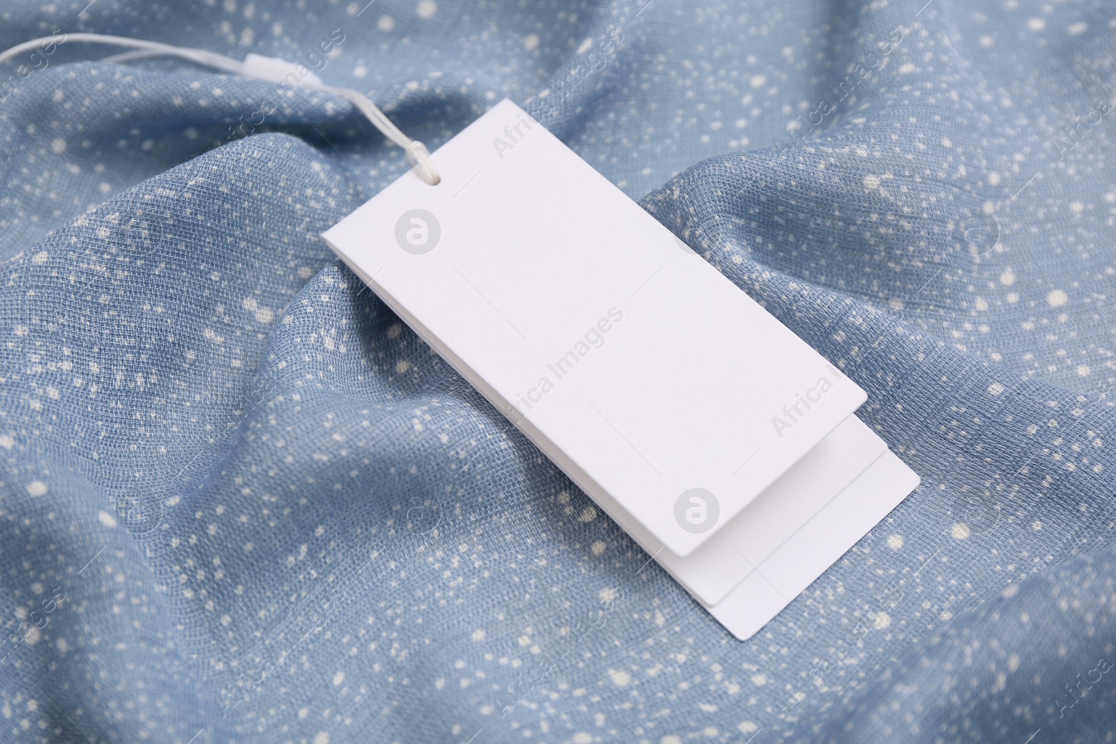 Photo of Blank white tags on light blue fabric, closeup. Space for text