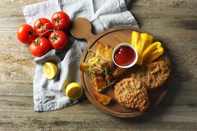 Photo of Tasty schnitzels served with potatoes, ketchup and vegetables on wooden table, flat lay