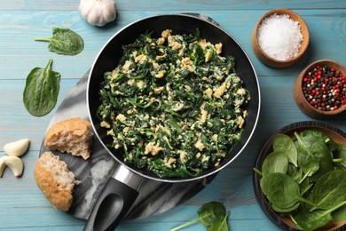 Photo of Tasty spinach dip with eggs in dish served on light blue wooden table, flat lay