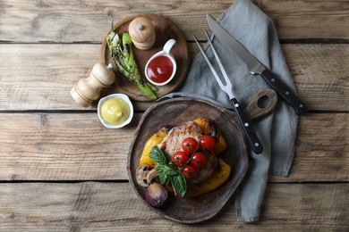 Photo of Delicious grilled meat and vegetables served with sauces on wooden table, flat lay