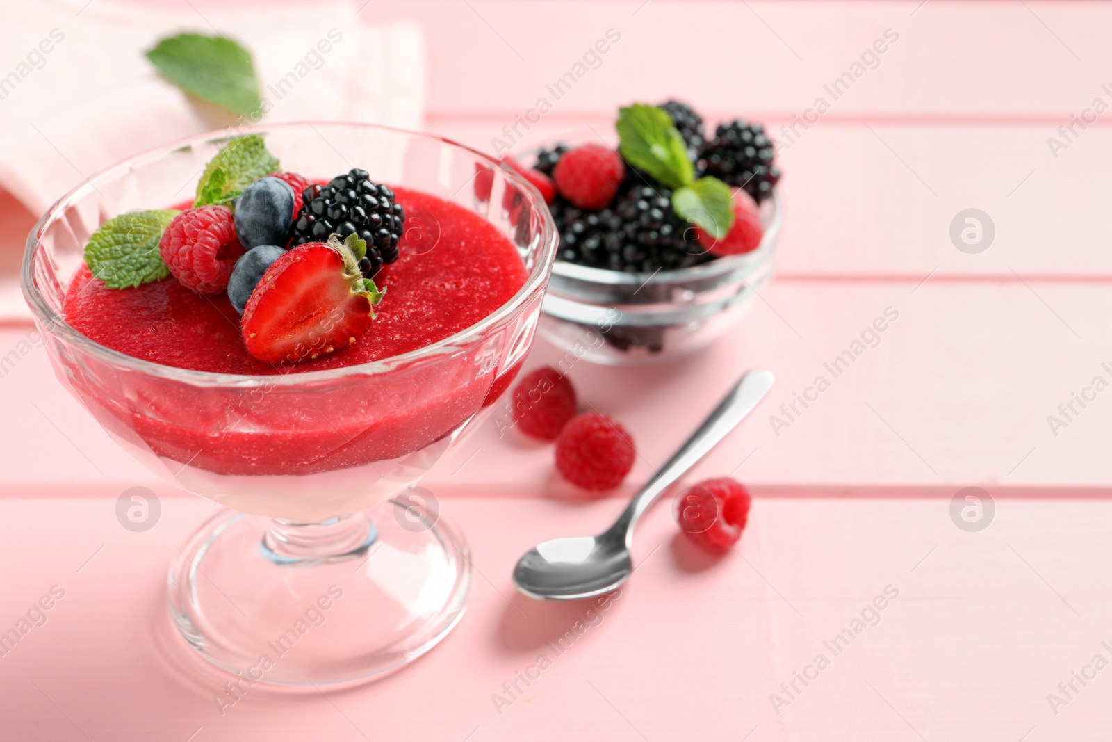 Photo of Delicious panna cotta with fruit coulis and fresh berries served on pink wooden table. Space for text