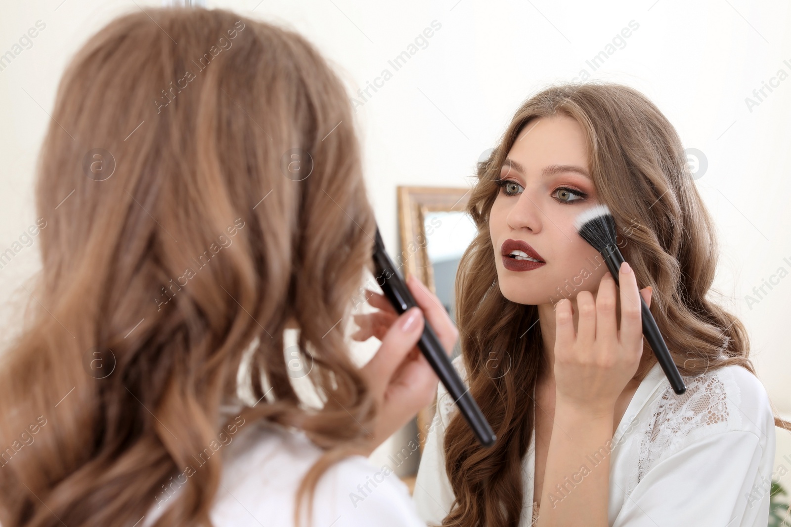 Photo of Young woman applying makeup near mirror in dressing room