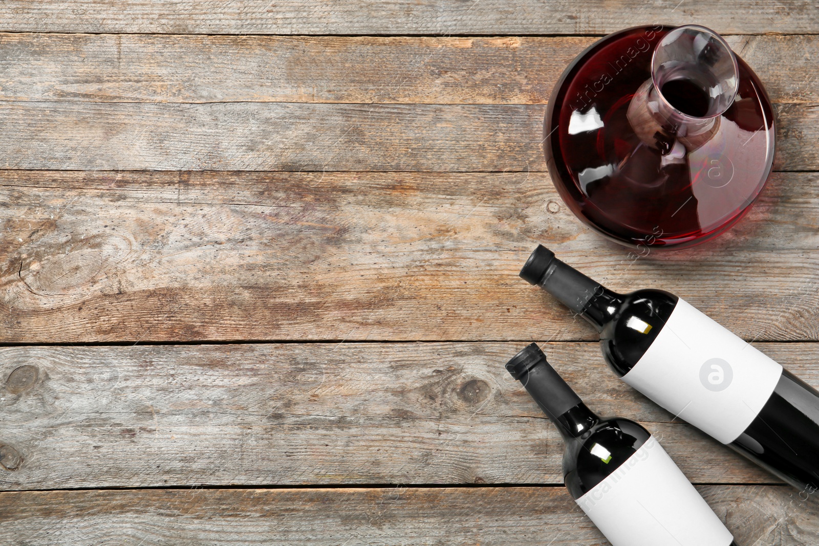 Photo of Decanter and bottles with red wine on wooden background, top view