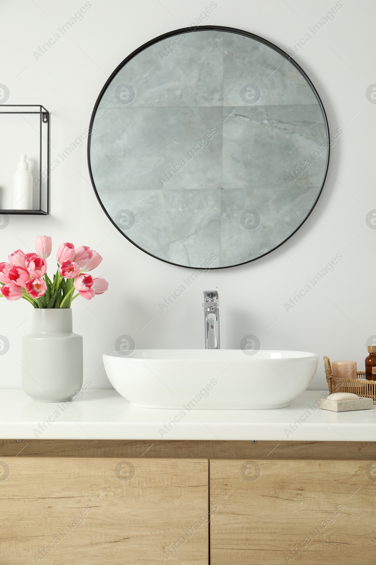 Photo of Vase with beautiful pink tulips and toiletries near sink in bathroom